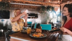 A woman photographing of her friend posing with her lunch at the Tiki Hut