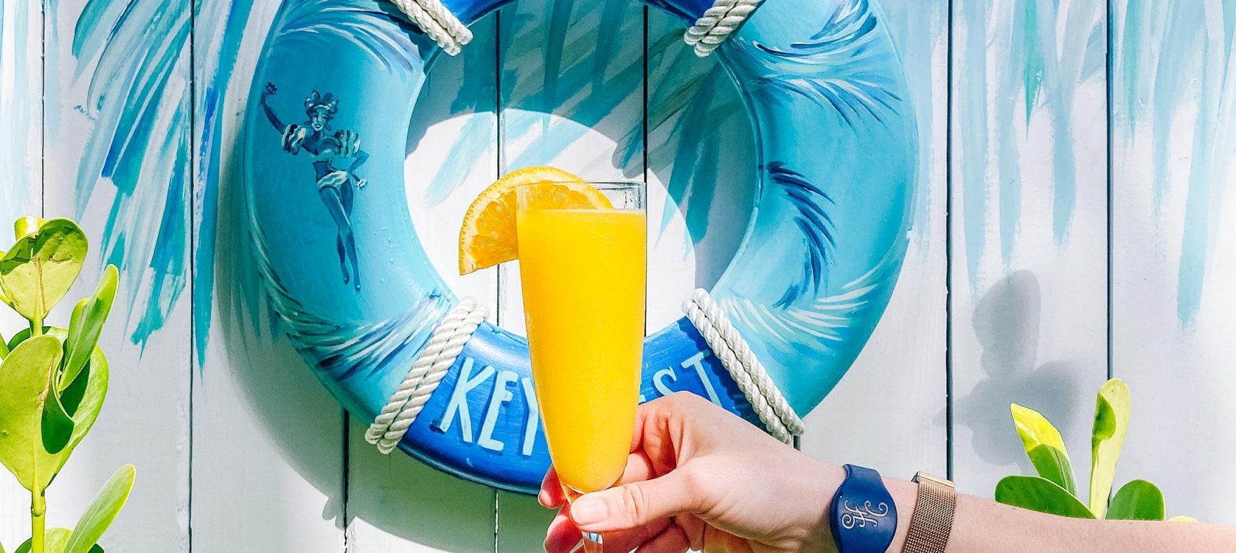 A hand holding a glass of mimosa against a background with an inflatable pool ring