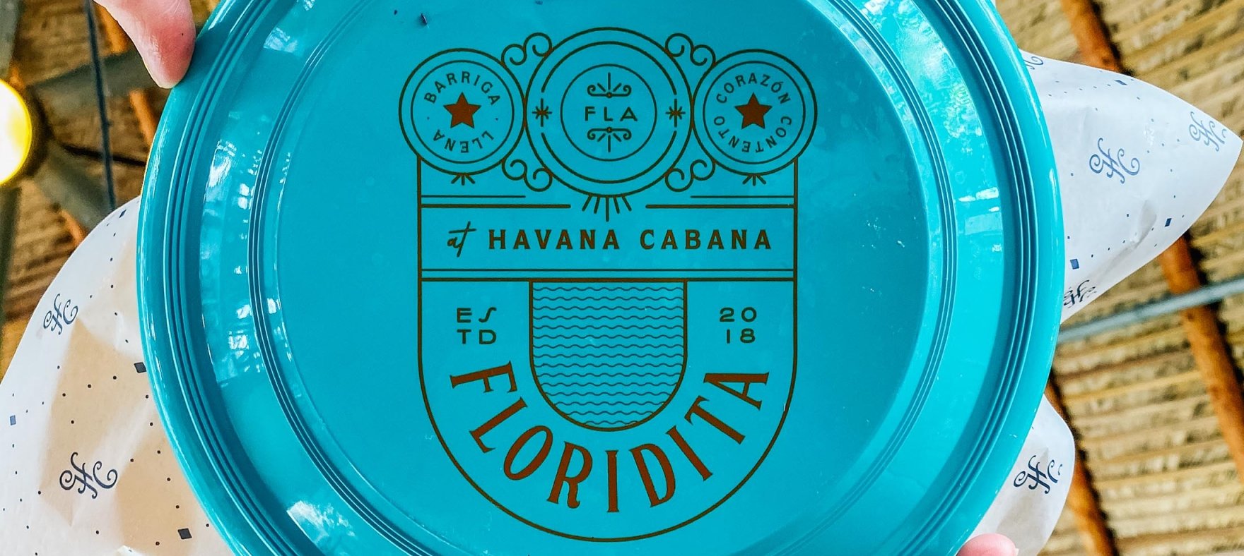 A low angle shot of the Havana Cabana Floridita logo on a plate raised by a pair of hands