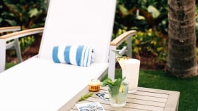 A rolled towel placed on a lounge chair next to a coffee table with a Mojito and a Pina Colada and collectable cards