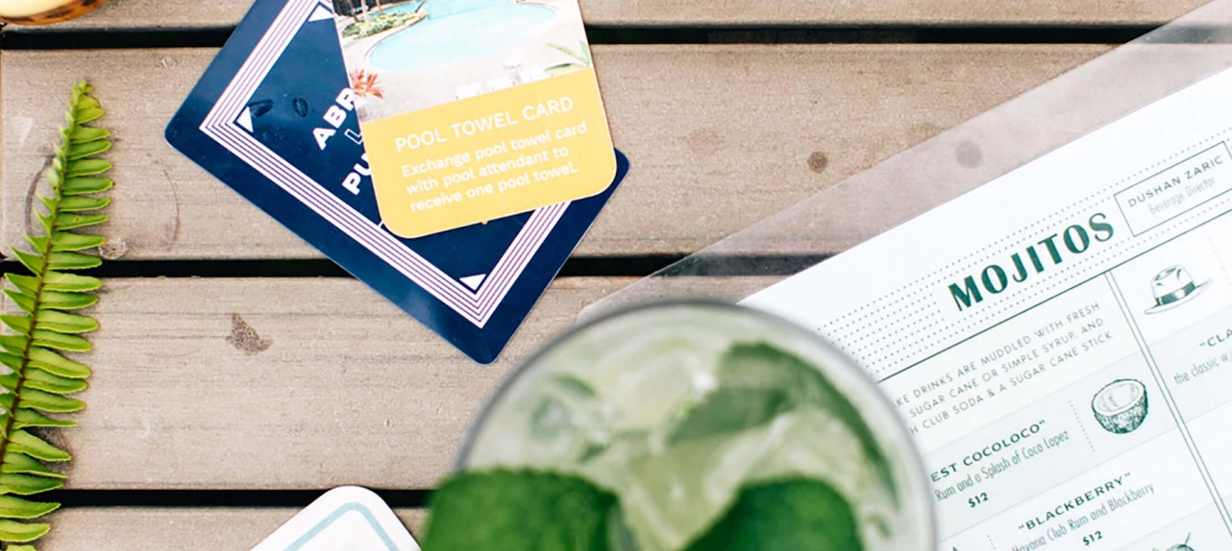 A glass of mojito is placed on top of a menu next to some cards and Pina Colada.