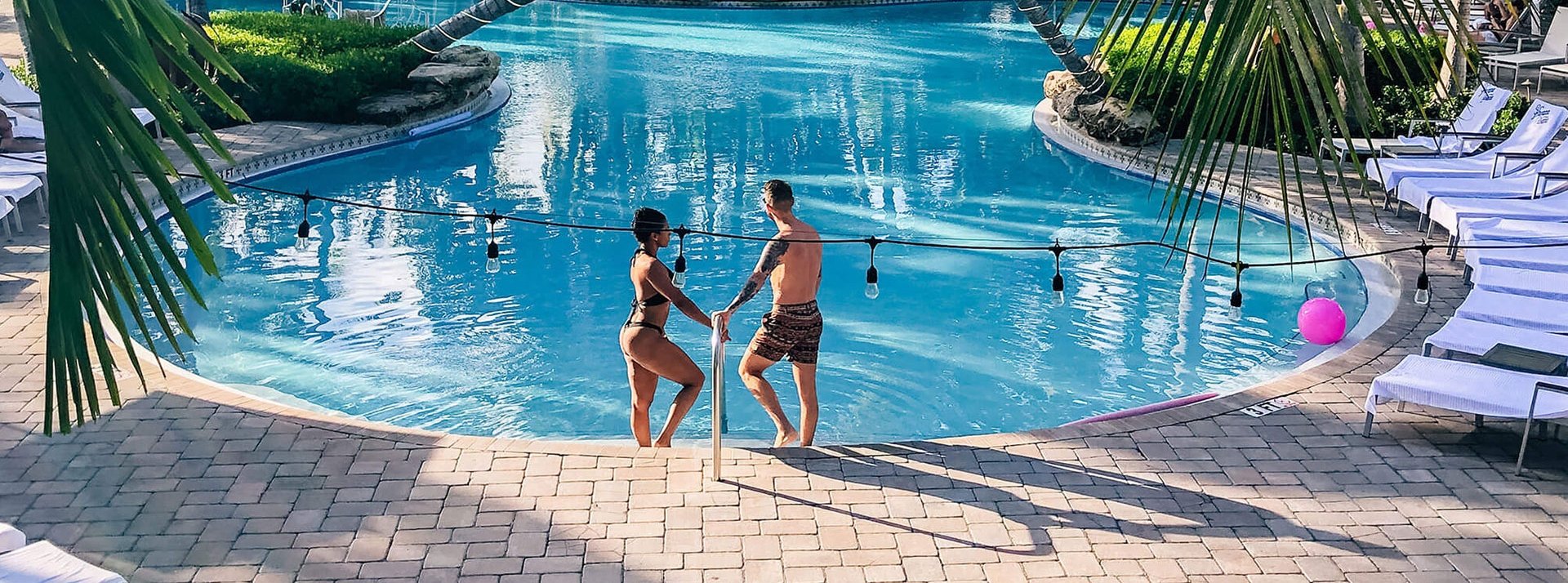A couple pose together at the edge of a resort pool.