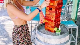 A vertical shot of a woman building a structure with mini bricks on top of a wooden barrel