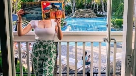 A vertical shot of a woman covering a face with a magazine as she poses in the balcony overlooking the outdoor pool