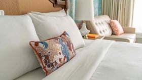 A soft focus on the pillows on the bed, next to the lamp on the side table overlooking the couch and curtain-drawn windows