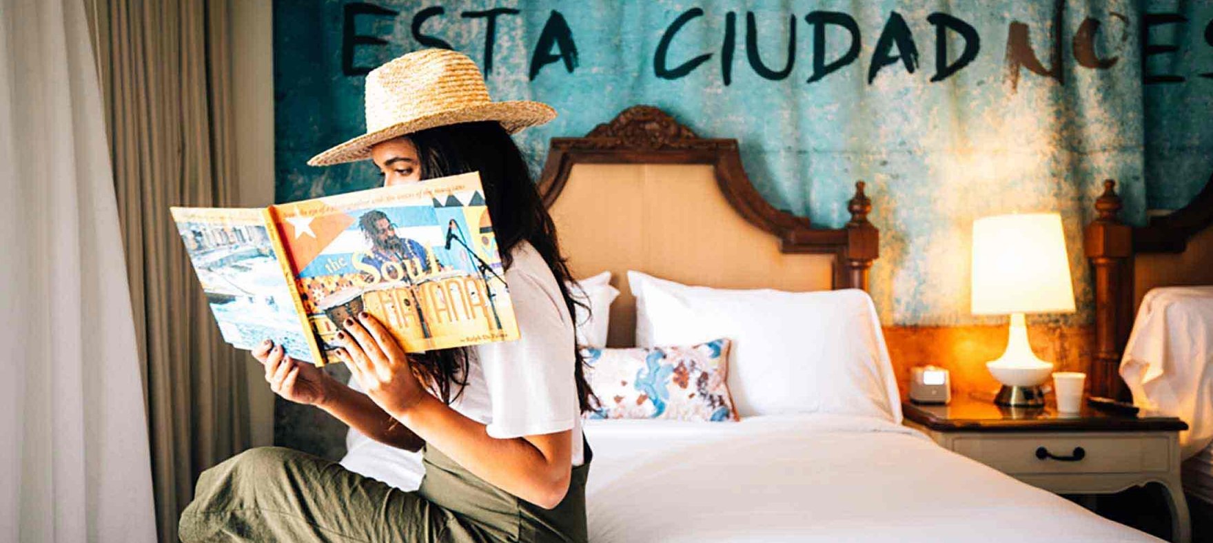A woman reads a magazine while sitting on a plush hotel bed at Havana Cabana