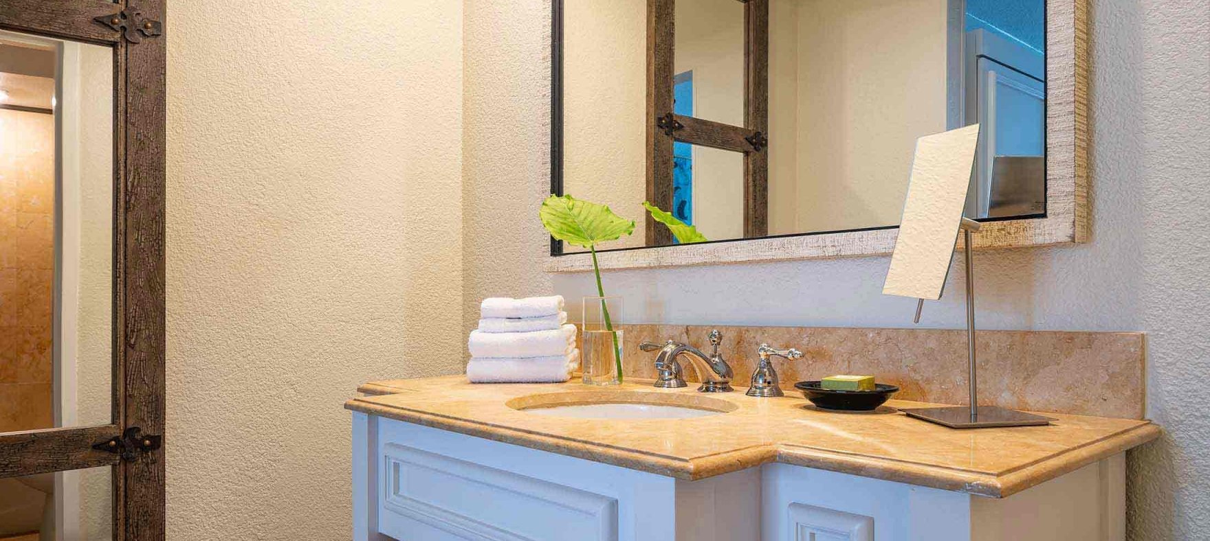 Stacked towels, and a vanity mirror placed on a spacious bathroom countertop with wooden shelves under a wide mirror