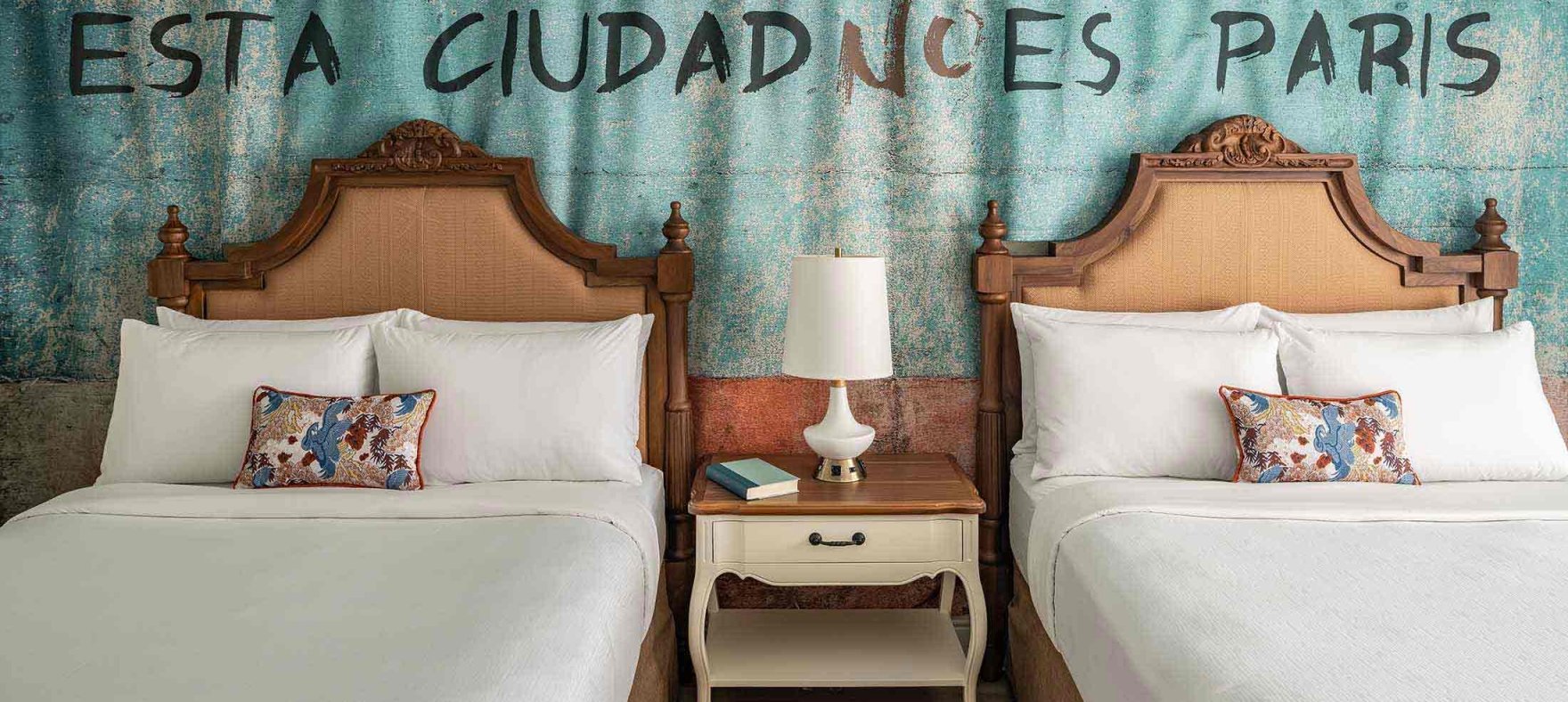 Two queen-side beds with a lamp placed on the shared bedside table in between