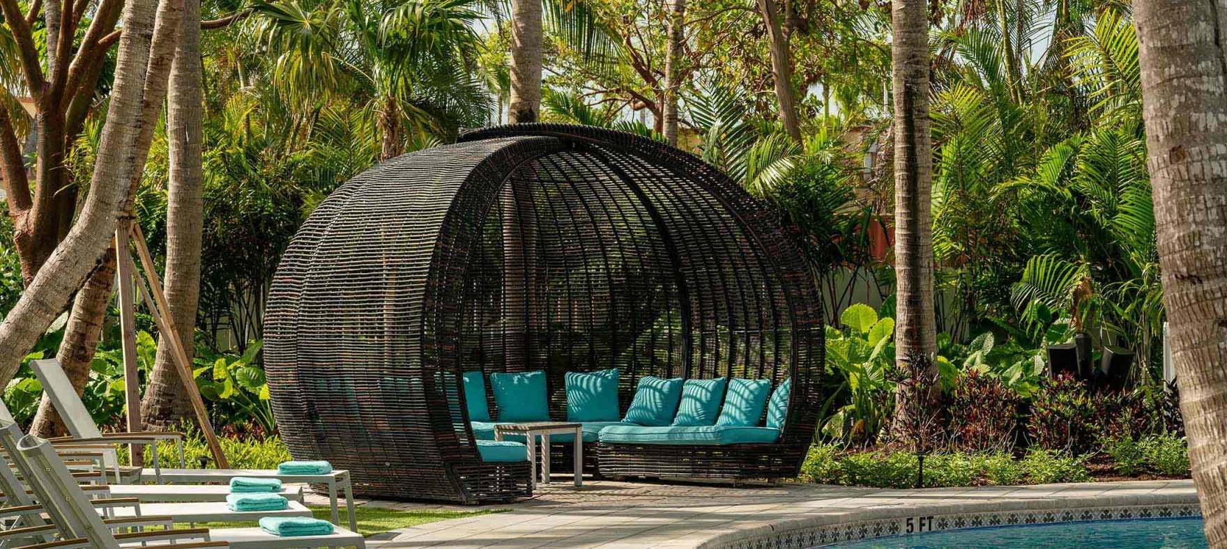 Lined lounge chairs next to the woven gazebo overlooking the pool