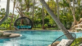 A hoop chair next to the swimming pool with a woven gazebo on the other end