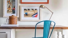 A wooden desk and metal chair facing a wall with framed art