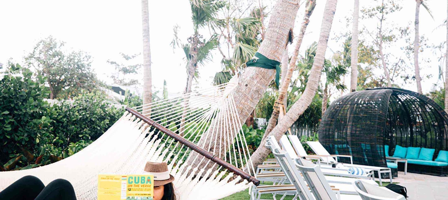 A woman reading a book while resting on a hammock next to the outdoor pool at Havana Cabana