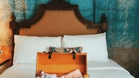 A vertical shot of opened luggage on a bed containing a cell phone, bikini, sandals, and more placed on a bed at a Havana Cabana room