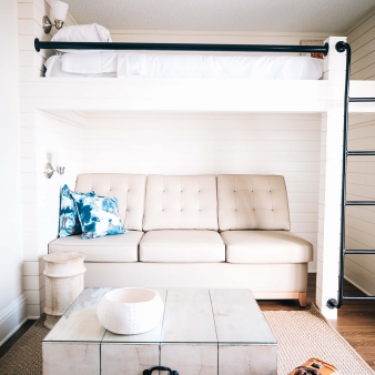 A leather couch next to a ladder leading to the bunk bed and facing the coffee table and arm chair on the opposite side