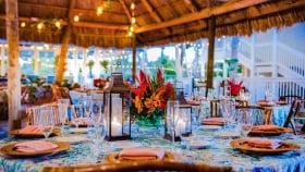 Table decor with napkins on plates, cutleries, champagne flutes and wine glasses, along with the candle lanterns and flowers in the center