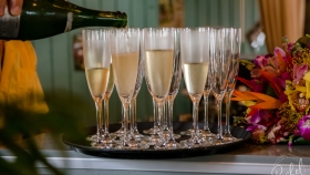 A close up of a hand pouring champagne into flutes set on the tray next to a floral bouquet