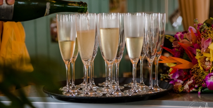 A close up of a hand pouring champagne into flutes set on the tray next to a floral bouquet