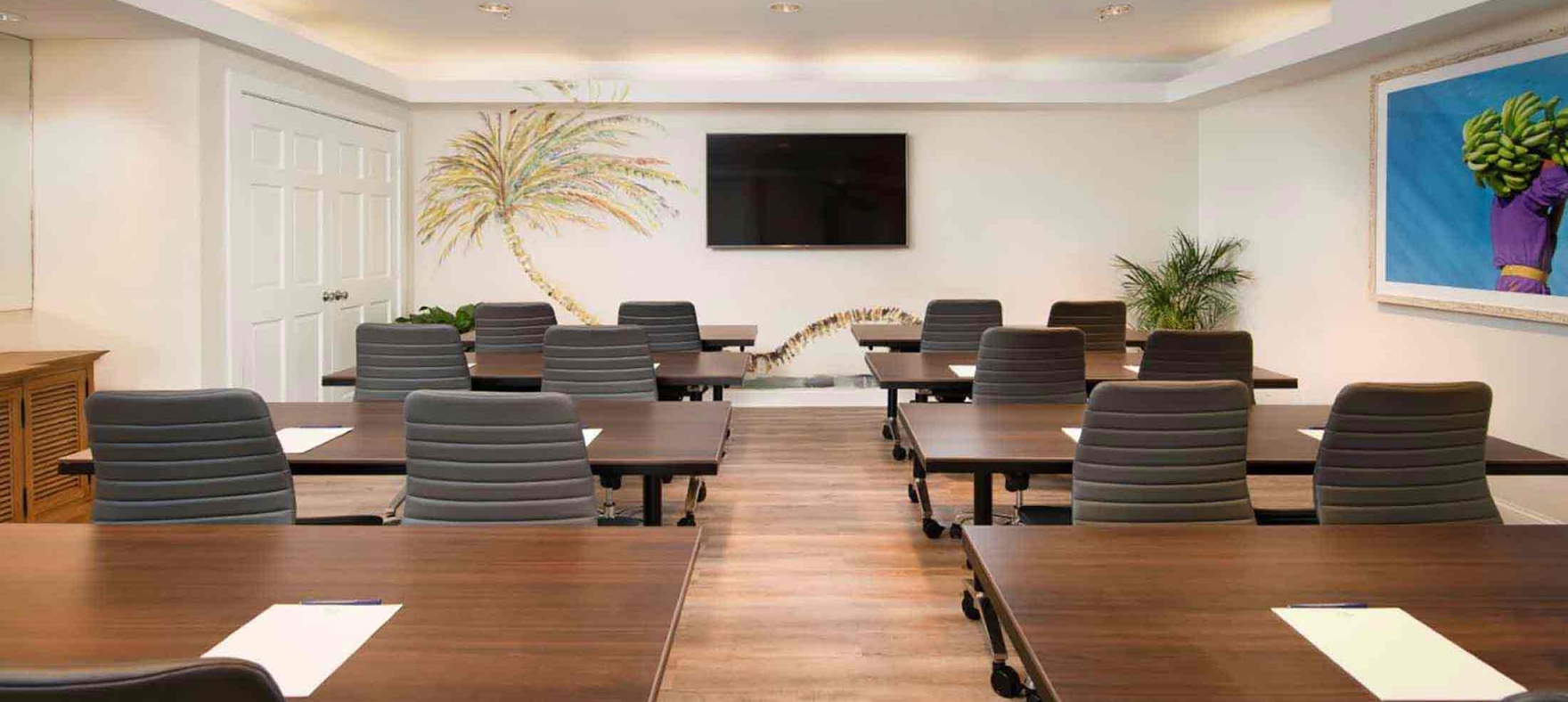A meeting room with tables set into two rows facing the television on the wall