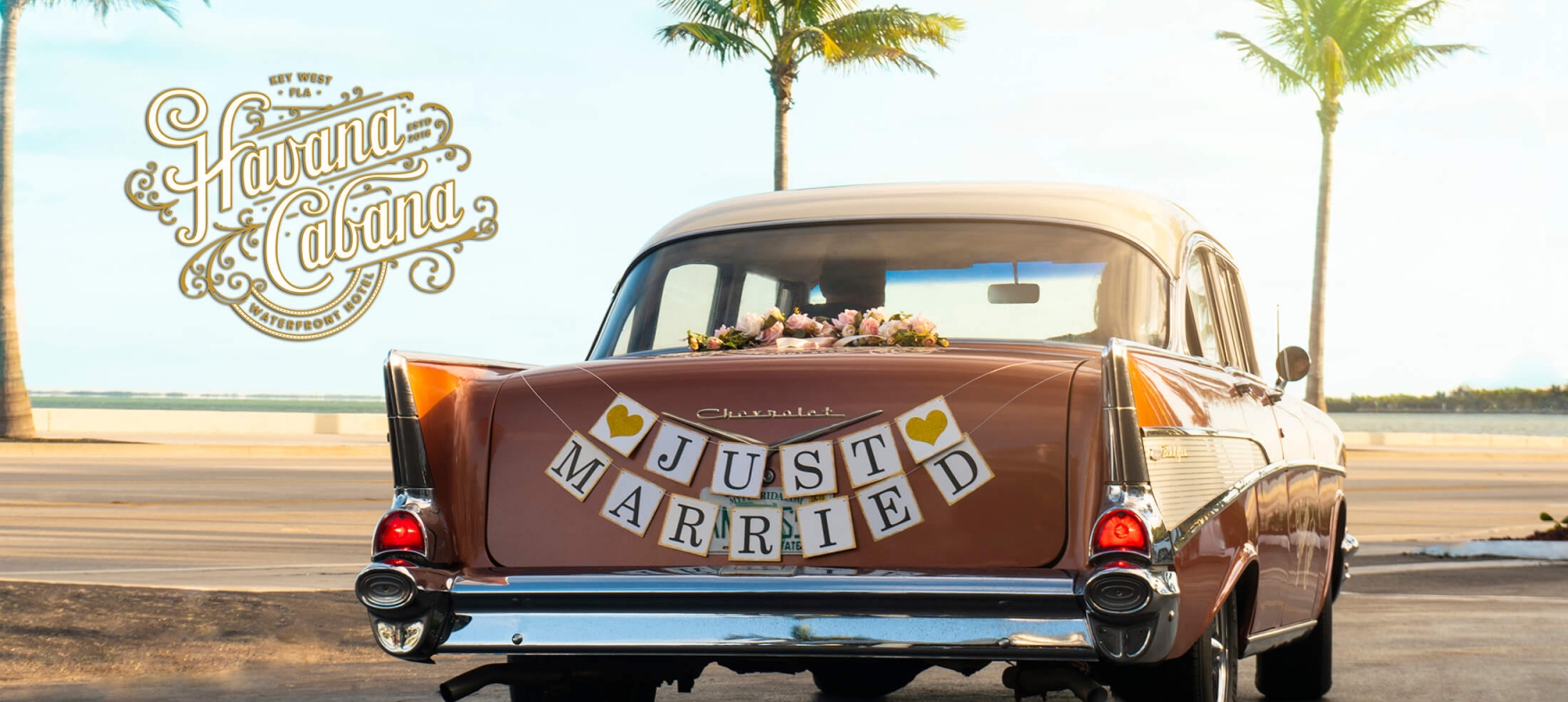 The back of a classic Chevrolet decorated with Just Married car banner and flowers