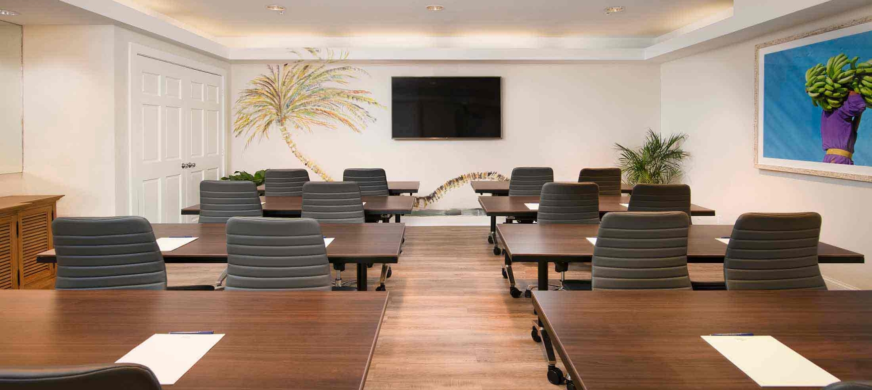 A meeting room with tables set into two lines facing the television on the wall