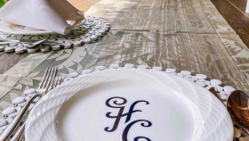 HC initialled dining plates set on a placemat with cutleries next to other plates with napkins and candle shades in the center