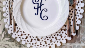HC initialled dining plates sitting on a placemat with cutleries on both sides set on a table overlooking a chair