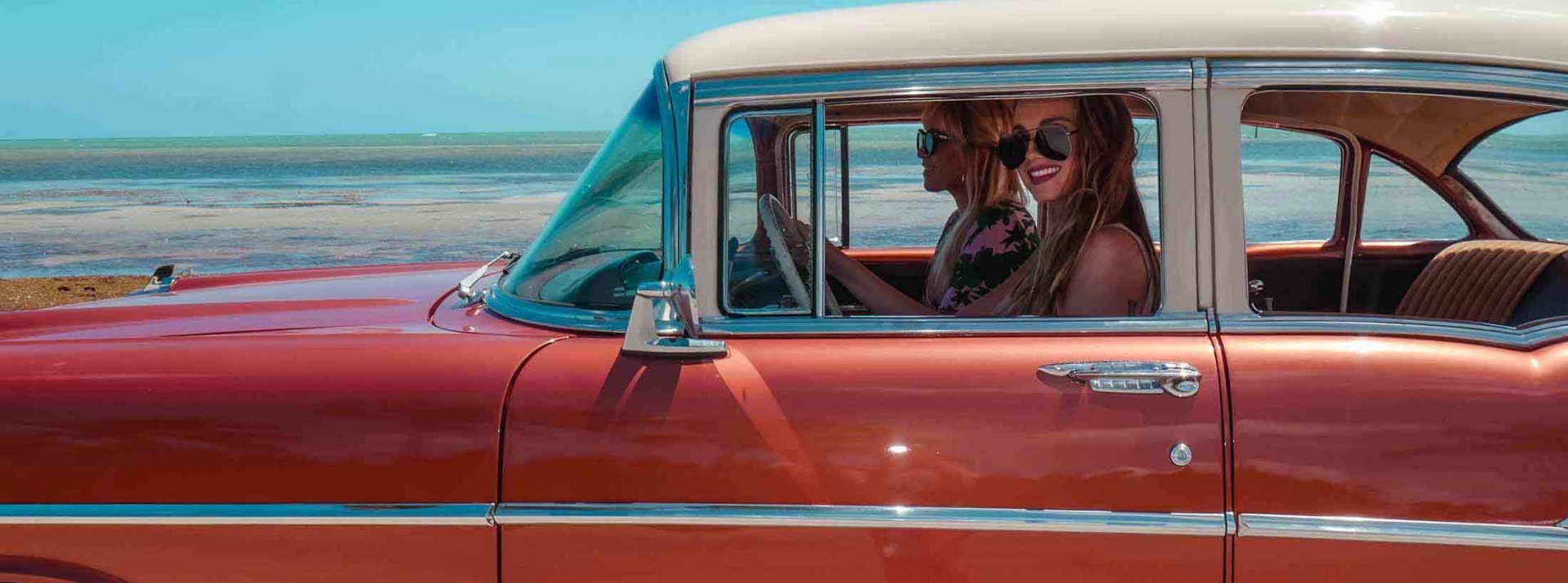 Two women driving a car smiling out the side window