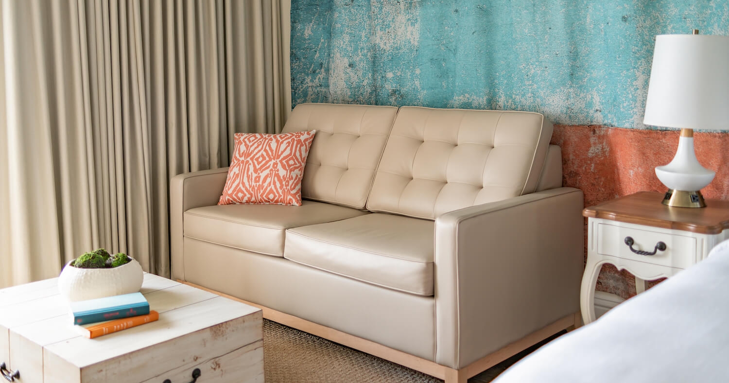 A beige couch equipped with an orange throw pillow.