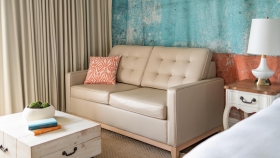 A beige couch equipped with an orange throw pillow.