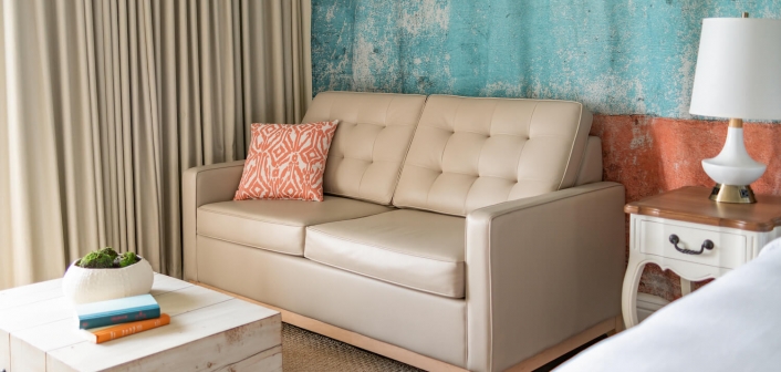 A beige couch equipped with an orange throw pillow.