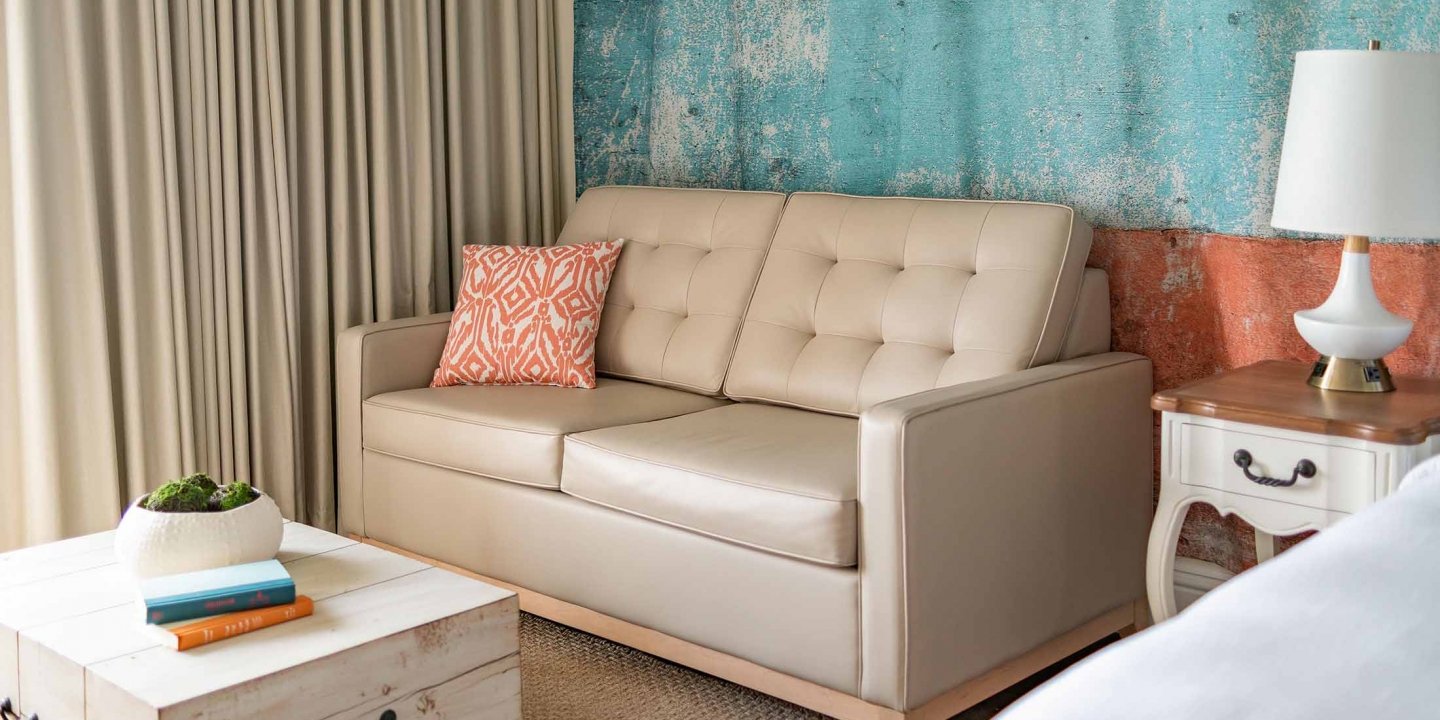 A close up of the leather couch with a decorative pillow facing the white-washed wooden coffee table
