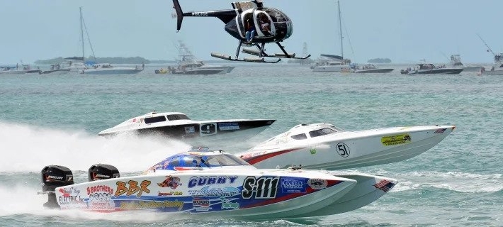 A few power boats on the water with a helicopter in the background
